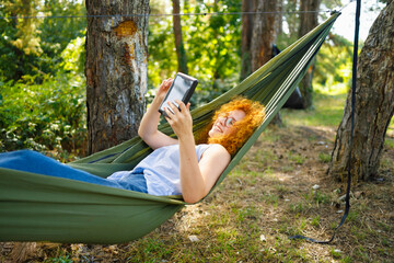 A woman laying in a hammock and buying online with her tablet