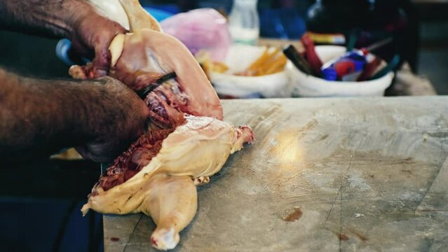 Hands of a caucasian man cutting chicken in the market. Cutting raw chicken into pieces