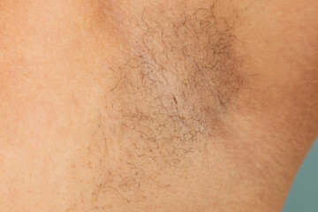 Person with hairy underarms closeup, free copy space, skin background. Arm with armpit hair. Female beauty trend, freedom, sensitive skin, growing body hair, feminism, body positive, naturalness.