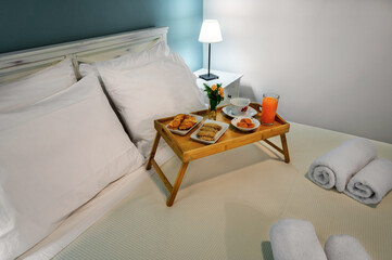 Fototapeta na wymiar Wooden small tray with breakfast and coffee on the bed. Selective focus. Bedroom concept.