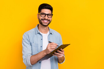 Obraz na płótnie Canvas Portrait of young smiling happy man writing paper pad work document isolated on yellow color background