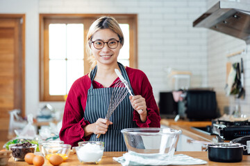 Beautiful young woman  is mixing batter, looking at camera and smiling while baking in kitchen at home ,decorating a cake of chocolate cake,cooking class, culinary, bakery, food and people concept