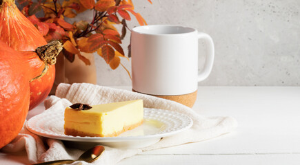 Pumpkin pie piece on white plate, cup of tea or coffee with pumpkins, colorful leaves. Copy space.