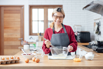 Beautiful young woman  is mixing batter, looking at camera and smiling while baking in kitchen at home ,decorating a cake of chocolate cake,cooking class, culinary, bakery, food and people concept