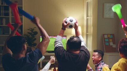 Happy Asian people with friends watching soccer or football on tv and celebrating victory at home, world cup football cheering concept