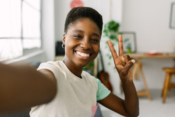 Cheerful young black african woman taking selfie portrait with phone at home office