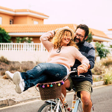 Two happy and active person man and woman enjoying bike ride together having fun and laughing a lot. Young mature couple use green eco transport. Male carrying female on a bike. People outdoor leisure