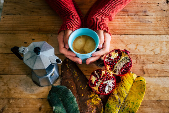 Autumn breakfast time concept lifestyle with above view of person holding a cup of hot moka italian traditional coffee on a wooden table with autumn decorations. Copy space image of people with cafe