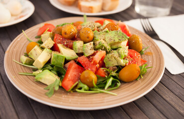 dish of fresh vegetables arugula, avocado, cherry tomatoes with olives on dining table