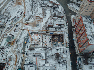 Construction of a new residential complex in winter. New housing. View of the construction site from above. Construction of a multi-storey building using a crane and concrete