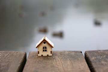 Wooden house model on old boards on blurred background of autumn lake with swimming ducks in fog....