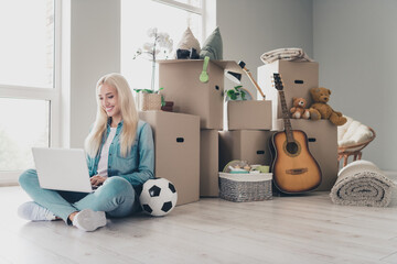 Photo of positive pretty young lady dressed denim shirt typing modern device moving new house indoors apartment