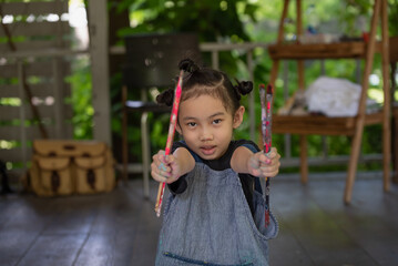 Cute little Asian girl showing paintbrush for paint a picture