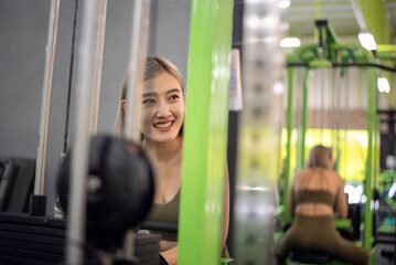 Fototapeta na wymiar Strong young Asian woman exercising with pulldown machine in a fitness club, doing exercises in gym