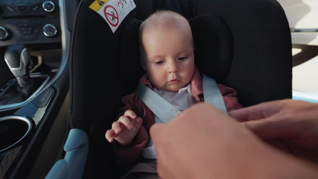 Close up father puts his little cute newborn baby in the car seat and fastens safety belts during a joint trip with a kid in the car. Kissing. Funny child. Childhood. Happy. Slow motion