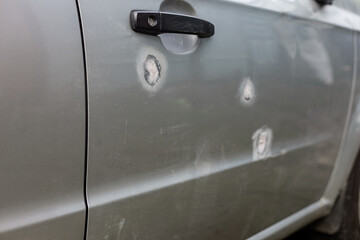 A part of a gray car damaged by fragments from military missiles, puttied parts, holes smeared with putty,