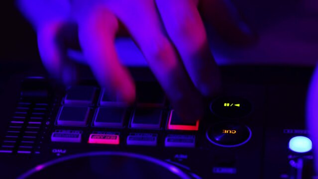 Top view. Close-up view of hands of dj maker making sounds at night club party with professional sound mixer in neon light. Modern party style. Deep beats.