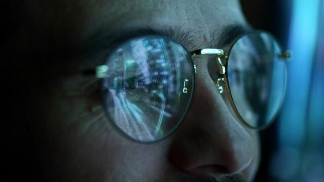 Close up view of man's eyes in eyewear looking at pc screen with computer reflection at eyeglasses. Using internet, working online, tracking database.