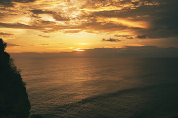 Beautiful sunset sunrise at the beach with dramatic clouds over the sea and red pink flowers in the foreground - Bali