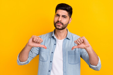Photo of sad young man wear denim shirt showing two thumbs down interested isolated yellow color...