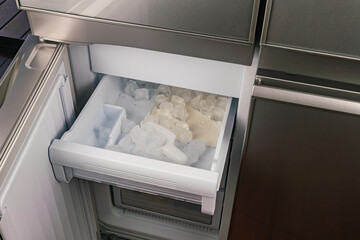 Ice cubes in the tray inside of automatic ice maker in a modern refrigerator.