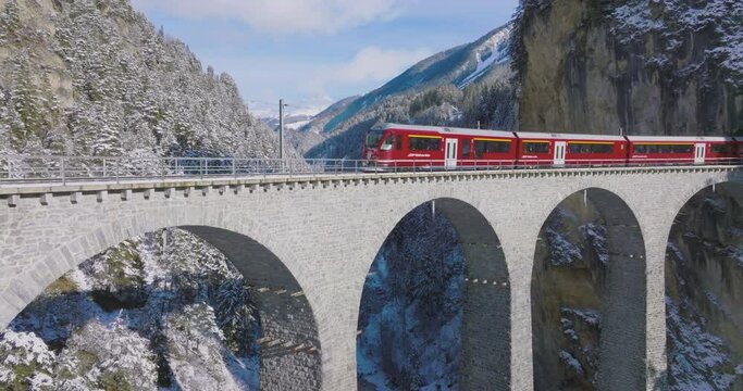 Landwasser Viaduct world heritage sight with luxury Glacier and Bernina express in Swiss Alps snow winter scenery. Aerial Drone shot red train passing through famous mountain in Filisur, Switzerland.