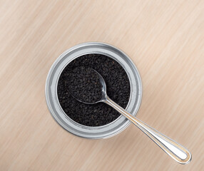 Top view of black sesame seeds in a jar and a metal spoon.