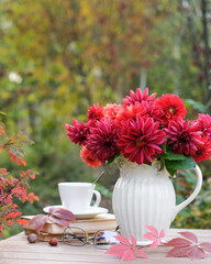 Obraz na płótnie Canvas Vase with red autumn flowers and books on the table in the autumn garden. Autumn still life