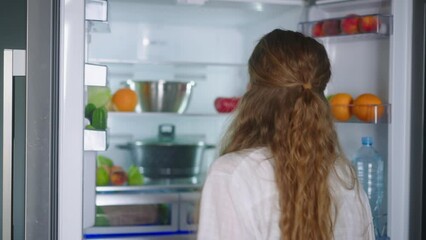 Young woman taking vegetables from fridge. Girl getting a tomato from refrigerator. Female having something healthy for snack. Pretty caucasian woman opening and closing fridge