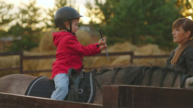 professional riding instructor is teaching little boy to ride horse, training in pony club for kids