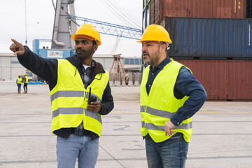 Two dock workers in reflective waistcoats and hard hats talking to each other outdoors
