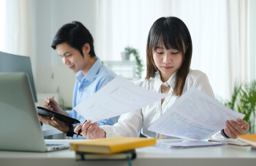 Pretty asian woman employee checking financial reports while sitting in office with her colleague.