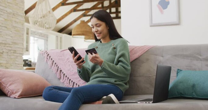 Biracial woman using smartphone and holding credit card in living room