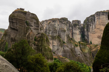 Plakat Panoramic view of unique rock formations near Holy Monastery of Varlaam on cloudy foggy day in Kalambaka, Meteora, Thessaly, Greece, Europe. Rocks overgrown with green moss creating moody atmosphere