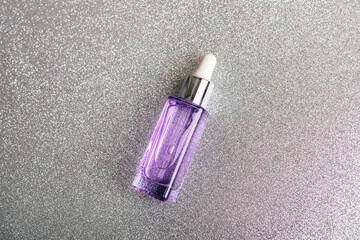 Cosmetic purple serum bottle on silver background. Skincare, spa and wellness concept. Top view,...