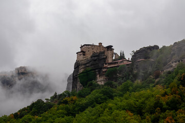 Fototapeta na wymiar Panoramic view of Holy Monastery of Varlaam and Monastery of Rousanou surrounded by misty fog on cloudy day, Kalambaka, Meteora, Thessaly, Greece, Europe. Dramatic landmark build on rock formations