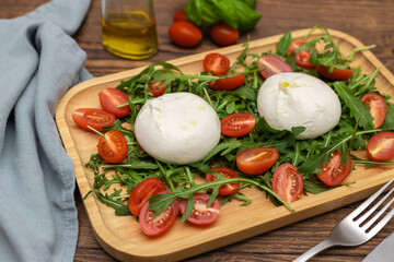Fresh traditional buratta cheese with arugula leaves and cherry tomatoes on a wooden tray. Italian cheeses