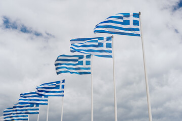 Fluttering row of Greek flags in the beautiful white clouds