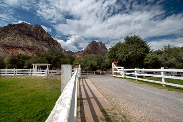 Fototapeta na wymiar Ranch road with white wooden fence leading to mountain trails