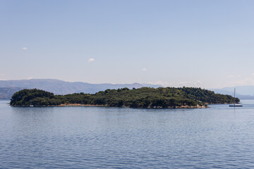 Fototapeta premium Protected nature reserve wooded uninhabited Ptichia island is located in the bay opposite Corfu Town, Ionian islands, Greece, background in summer haze