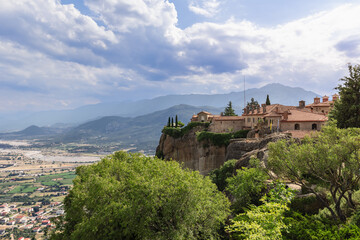 Fototapeta na wymiar Panoramic view of ancient St. Stephen Holy Monastery with unique sheer cliffs and dense green forest in Thessaly plain, Meteora, Greece