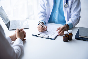 Doctor and patient sitting and talking at medical examination at hospital office, close-up. Therapist filling up medication history records. Medicine and healthcare concept.