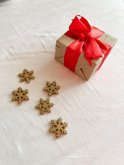 A gift with a red bow and golden snowflakes lie on a white fabric surface. Copy space.