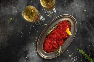 Red caviar filling metal plate and a glass of champagne on a stone background. Gourmet food close up, appetizer, selective focus, place for text - obrazy, fototapety, plakaty