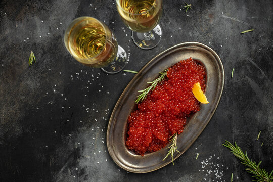 Red caviar filling metal plate and a glass of champagne on a stone background. Gourmet food close up, appetizer, selective focus, place for text