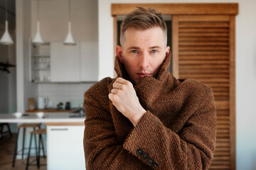 a man in a warm coat trying to keep warm at home. Home heating shutdown concept. Gas shutdown.