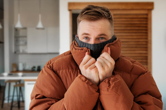 A Man In A Warm Down Jacket Trying To Keep Warm At Home. Home Heating Shutdown Concept. Gas Shutdown.