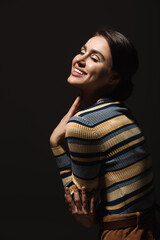 cheerful young woman in striped turtleneck smiling isolated on black.