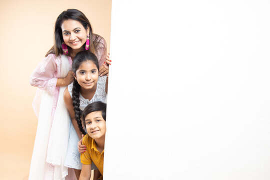 Advertising. Portrait of happy indian mother with two kids standing with big white empty banner or poster billboard for content, place for text or image isolated on plane studio background