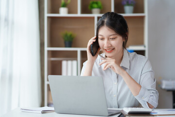 Charming and smiling Asian business woman Talk to customers on mobile phones and use their laptops to do office work.